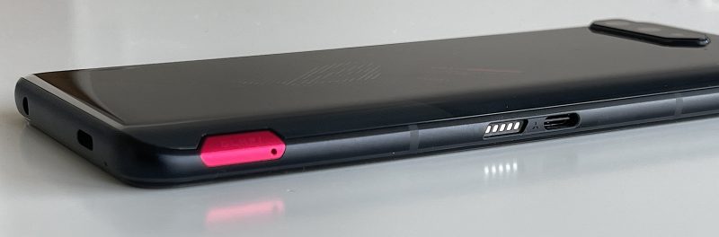 ROG Phone 5:n pää-USB-C-liitäntä nopeimmalla lataus- ja tiedonsiirto- sekä DisplayPort-tuella löytyy puhelimen kyljeltä. Sen rinnalla on POGO-pinniliitäntä tuuletinlisävarusteelle. Erottuva punainen kohta kyljellä on SIM-korttikelkka.